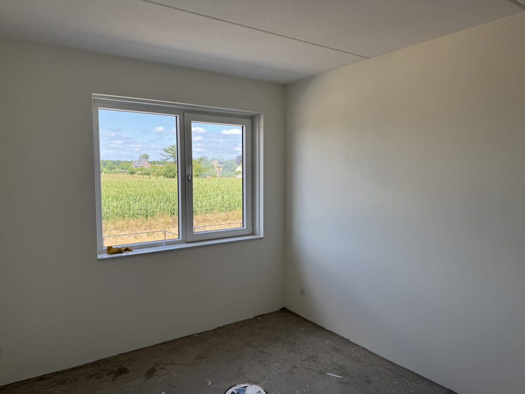Lege slaapkamer in een nieuwbouwhuis met gladde lichte wanden en een raam met uitzicht op het land